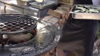 Aşçı kabakları kızartıyor. Izgara sebze. Yuvarlak kase şeklinde ızgara ve içinde ateş var.. 