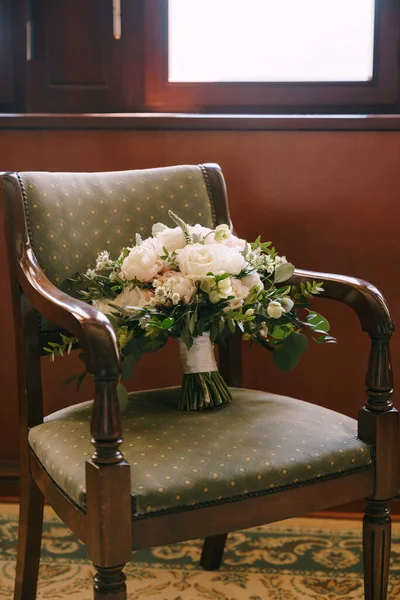 Ramo nupcial de peonías blancas, rosas, verónica y ramas de eucalipto en un sillón de madera con tapicería de satén verde — Foto de Stock