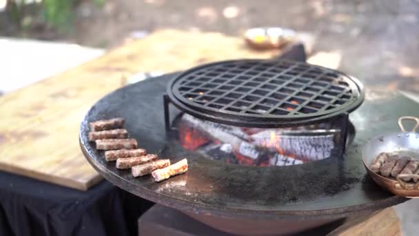 Srbské národní jídlo - chevapchichi. Masové párky se smaží na plochém grilu s ohněm uprostřed. — Stock video