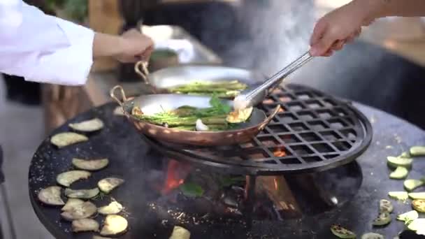 El cocinero tuesta los calabacines. Verduras a la parrilla. Parrilla redonda en forma de tazón con un fuego en el interior . — Vídeos de Stock