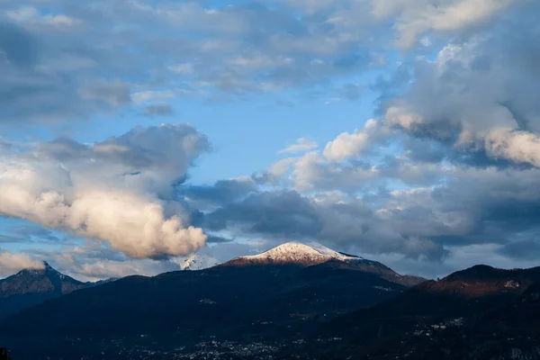 Der schneebedeckte Gipfel des Berges wird von der Sonne erleuchtet, die samtenen weißen Wolken am blauen Himmel über dem Comer See in Italien. — Stockfoto