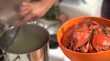 Aşçı, pişmiş kırmızı mavi yengeçleri tavadan çıkarıp turuncu bir kaseye koyar..