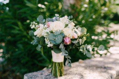 Taş çitin üzerinde pembe ve beyaz şakayık demeti, güller, okaliptüs ağacı dalları, Veronica, matthiola ve beyaz kurdeleler.