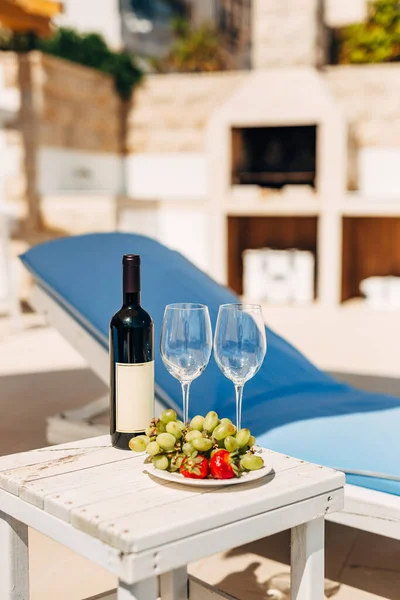 Une bouteille de vin, deux verres et des fruits sur la plage près du transat. A l'ombre d'un parapluie, dans la villa. — Photo