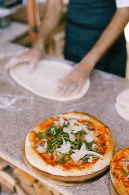 Pizzayı peynirli ve roka ile hazır et. Şefin arka planında pizza pişir. Hamuru masanın üzerine bırak..