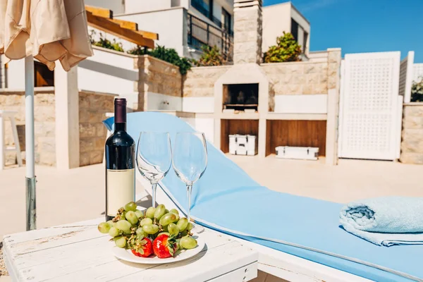 Une bouteille de vin, deux verres et des fruits sur la plage près du transat. A l'ombre d'un parapluie, dans la villa. — Photo