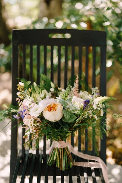 Ramo nupcial de rosas crema, peonías rosadas, eustoma, cera, astilbe, limonio, ramas de eucalipto, mattiola, espárragos con cintas de crema en la silla negra al aire libre —  Fotos de Stock