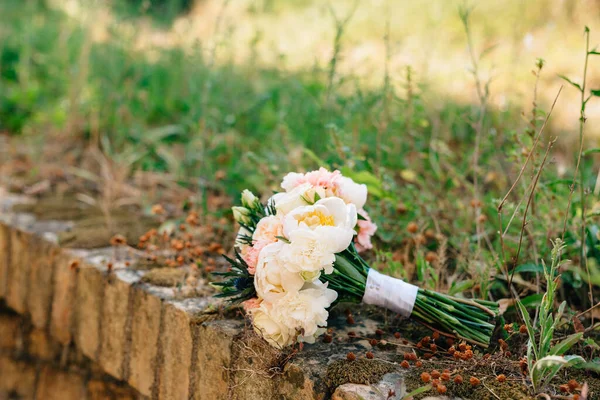 Buquê nupcial de peônias brancas e rosa, eríngio e botões verdes, com fitas brancas para baixo na grama — Fotografia de Stock