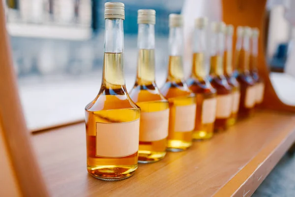 Üvegek egy arany alkoholos itallal. Üres címkék. Rakia üvegei egymás után vannak kiállítva.. — Stock Fotó