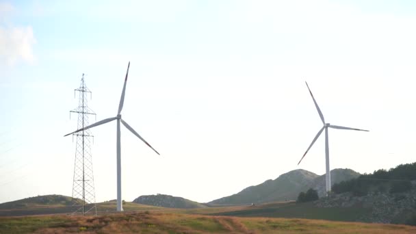 Duas enormes turbinas eólicas entre as colinas verdes contra o céu nublado . — Vídeo de Stock