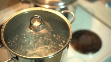 Mutfak sobasında kaynar su olan krom metal bir tava..