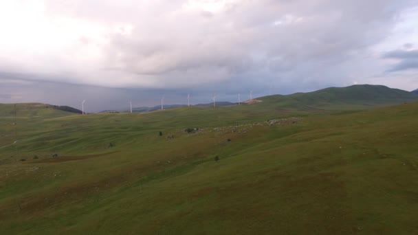 Tepelerdeki yeşil tarlalar ve ufuktaki rüzgar tarlaları. — Stok video
