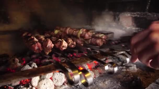 Les mains des chefs retournent les brochettes avec un kebab sur le gril sur les charbons en feu. — Video