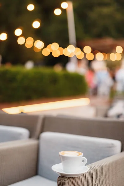 Secangkir kopi di sebuah kursi di sebuah restoran dengan latar belakang lampu-lampu karangan bunga. — Stok Foto