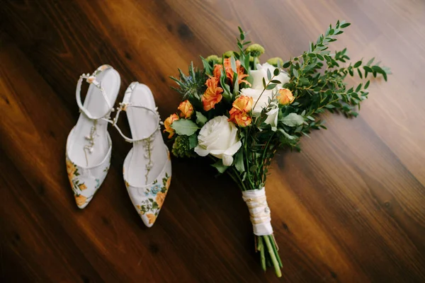Ramo nupcial de rosas blancas y naranjas, eringio, ammi, ramas de boj, alstroemeria con cintas blancas y zapatos de la novia en el suelo —  Fotos de Stock