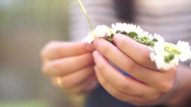 Kadınların ellerinin yakın plan çekimi. Bir kız papatya çelengi dokuyor.