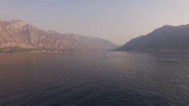 Karadağ 'ın Kotor Körfezi' nde yelken açan yat, gün batımıyla aydınlanan dağların arka planına karşı..
