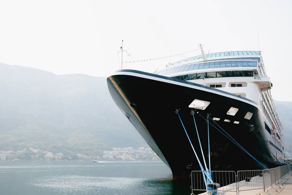 De neus van een close-up cruiseschip afgemeerd op een steiger in de buurt van de oude stad Kotor in Montenegro. In de baai van Kotor, tegen de achtergrond van bergen en bewolkte lucht. — Stockfoto