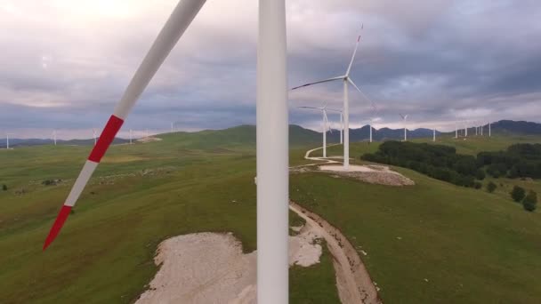 İnsansız hava aracının hava fotoğrafı - Karadağ 'ın dağlarındaki yeşil çayır ve tepelerin arka planına karşı dev bir rüzgar jeneratörü. — Stok video