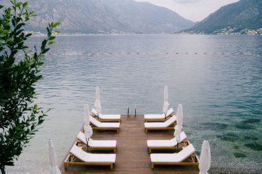 Karadağ 'ın Kotor Körfezi' ndeki rıhtımda güzel beyaz şezlonglar ve plaj şemsiyeleri.