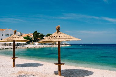 Hırvatistan 'ın Primosten kenti yakınlarındaki kumlu bir plajda iki adet plaj şemsiyesi. Mavi gökyüzü ve gök mavisi su. Cennet konsepti dinlenme.