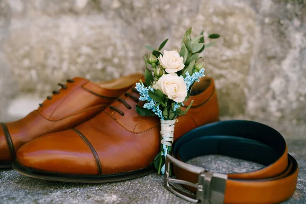 Stylish accessories for the groom, brown shoes, belt and bud on a mother-of-pearl background.
