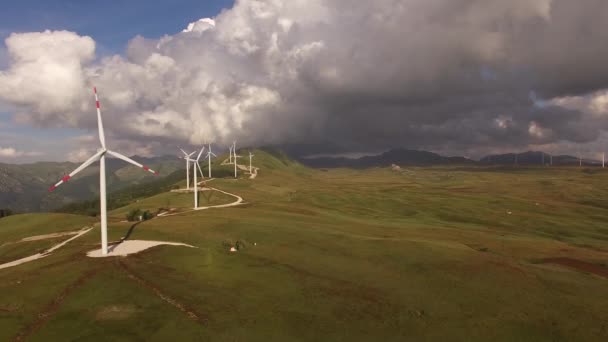 Zdjęcie lotnicze z drona - seria ogromnych turbin wiatrowych wzdłuż drogi na wzgórzu pośród gór w Czarnogórze. — Wideo stockowe