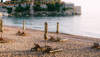 Karadağ 'da Sveti Stefan adası yakınlarındaki kumlu bir plajda plaj şemsiyeli ahşap şezlonglar.