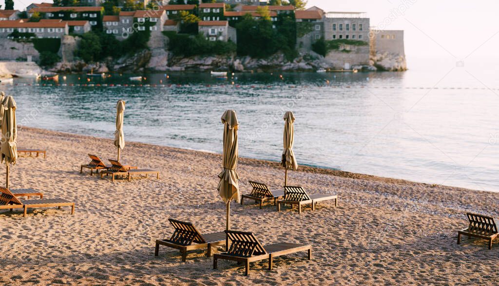 Wooden loungers with beach umbrellas on a sandy beach in Montenegro, near the island of Sveti Stefan.