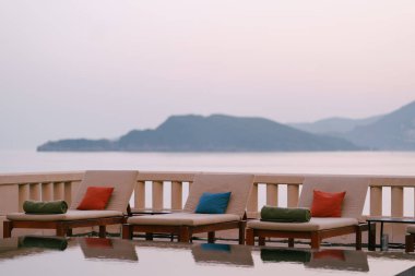 Güneş batarken, deniz kenarındaki villadaki havuzun yanındaki tahta şezlonglar..