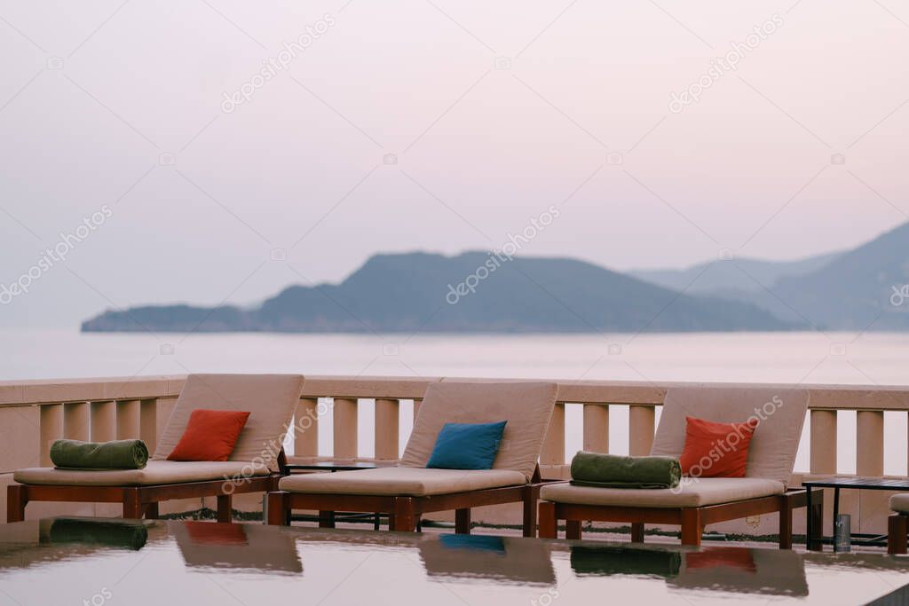 Wooden loungers near the pool at the villa by the sea, at sunset.
