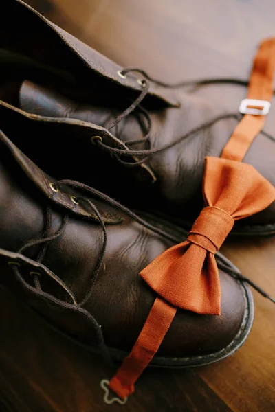 Zbliżenie pomarańczowej muszki pana młodego na brązowych męskich butach z rozwiązanymi sznurówkami na parkiecie. — Zdjęcie stockowe