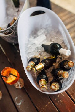 Tivat, Karadağ - 29 Temmuz 2020: Tahta bir yüzey üzerinde bir bardak portakal suyu ve bir dilim limon ile buz kovalarında dolu bira şişeleri.