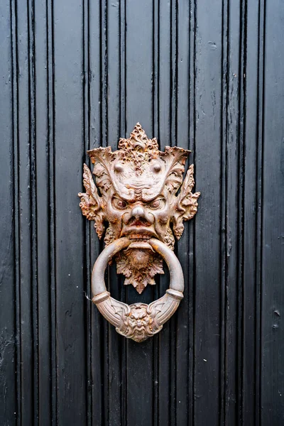 Antique door handle in the form of a demonic image with a ring in the mouth in gilding