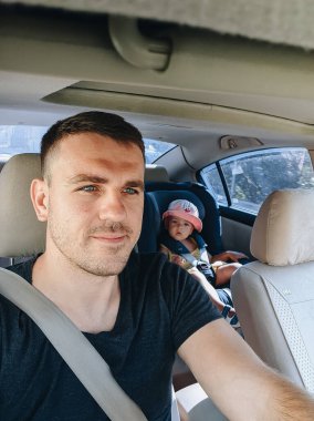 Baba ve kızı arabada. Araba süren bir adam. Çocuk arabası koltuğundaki küçük kız..