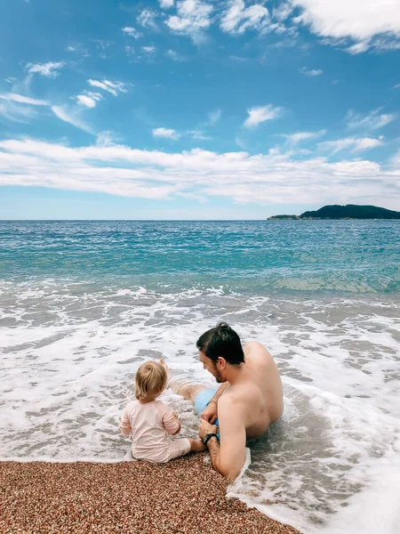 Ayah dan putrinya terbaring di ombak laut, di pantai berpasir di Montenegro, di Laut Adriatik. — Stok Foto