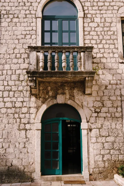 Entrada desde puertas de cristal verde a un antiguo edificio de ladrillo bajo un balcón con columnas. — Foto de Stock
