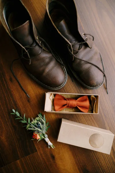 Krawat w pudełku dla pana młodego z butonierką i męskie buty z rozwiązanymi sznurowadłami na brązowej podłodze. — Zdjęcie stockowe