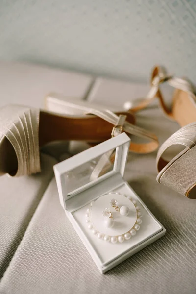 Перламутровые женские сандалии и коробка с браслетом из белых бусин и сережек. — стоковое фото