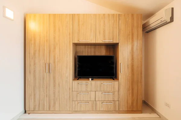 Televisor en un nicho en un gran armario de madera en una habitación luminosa con aire acondicionado. —  Fotos de Stock