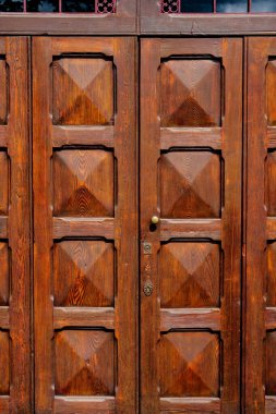 Kahverengi ahşap kapılar, girişteki metal ızgaranın altında kareler var..