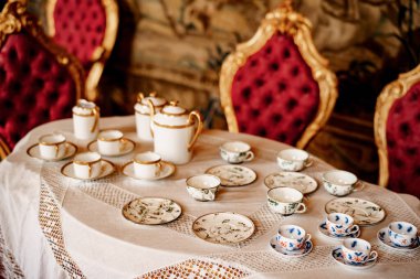 Mavi desenli bir çay seti ve beyaz şömine rafındaki bir tepside altın bir set. Kırmızı bir duvarın arka planında kalıplar var..