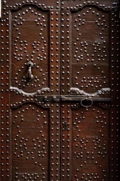 Brown wooden doors with many metal rivets and carvings with a long bolt and door knocker. — Stock Photo, Image