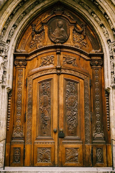 여러 개의 오래 된 조상이 있는 아치 아래 조각 된 형상, 설계 및 상징물이 있는 육중 한 나무로 된 문들. — 스톡 사진