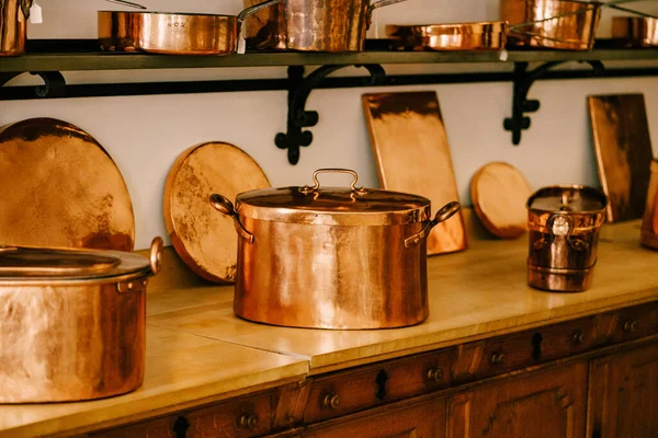 Large copper pots with hot coasters on the countertop with copper saucepans and saucepans on shelves to be attached to the white wall.