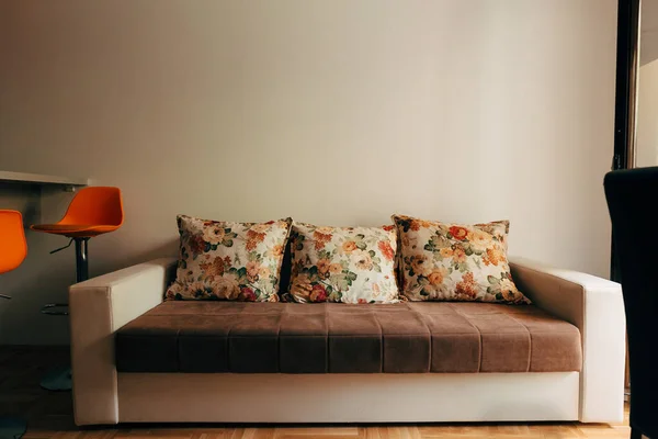 一个柔软的可兑换沙发，有三个枕头，房间里有橙色条凳，背景浅灰色. — 图库照片
