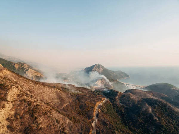 Die Stadt an der Küste Montenegros steht in Flammen. Weißer Rauch über der Stadt, der Straße und den Bergen. — Stockfoto