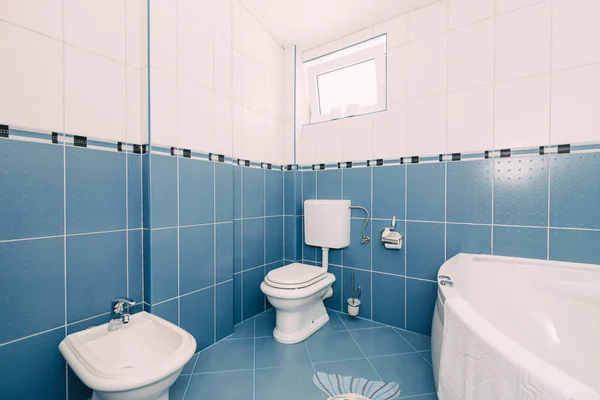 Bellagio, Italien - 07 juni 2020: Ett blått badrum med toalett, handfat, badkar och ett fönster öppet för ventilation. — Stockfoto