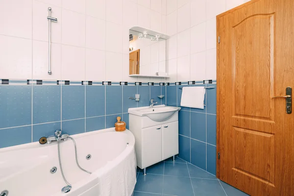 Badrum med hydromassage badkar, handfat med spegel och brun trädörr. — Stockfoto