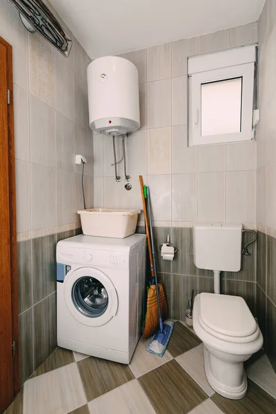 Toilet, washing machine, boiler, bowl, broom and mop in the bathroom.